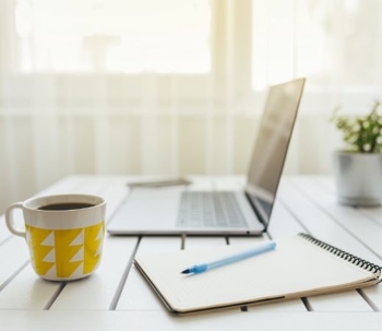 a laptop, pen, notebook, and coffee on a table